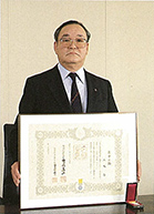 三木プーリの沿革写真 黄綬褒章を受章した三木齋副会長（勲章と表彰状を手にした受章記念の様子）